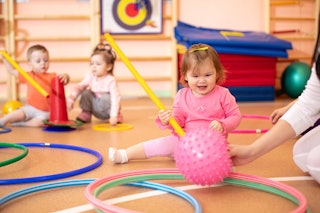 Daycare age children sitting on the floor of a gymnasium playing with hula hoops and sensory toys.